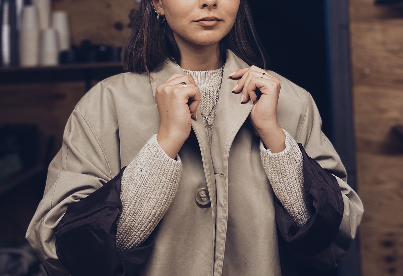 Person in a beige coat layered over a textured knit sweater, an example of muted layered acubi-style dressing