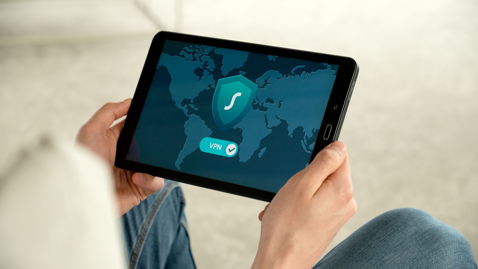 Person holding a tablet that shows a shield icon and a VPN connected switch over a world map