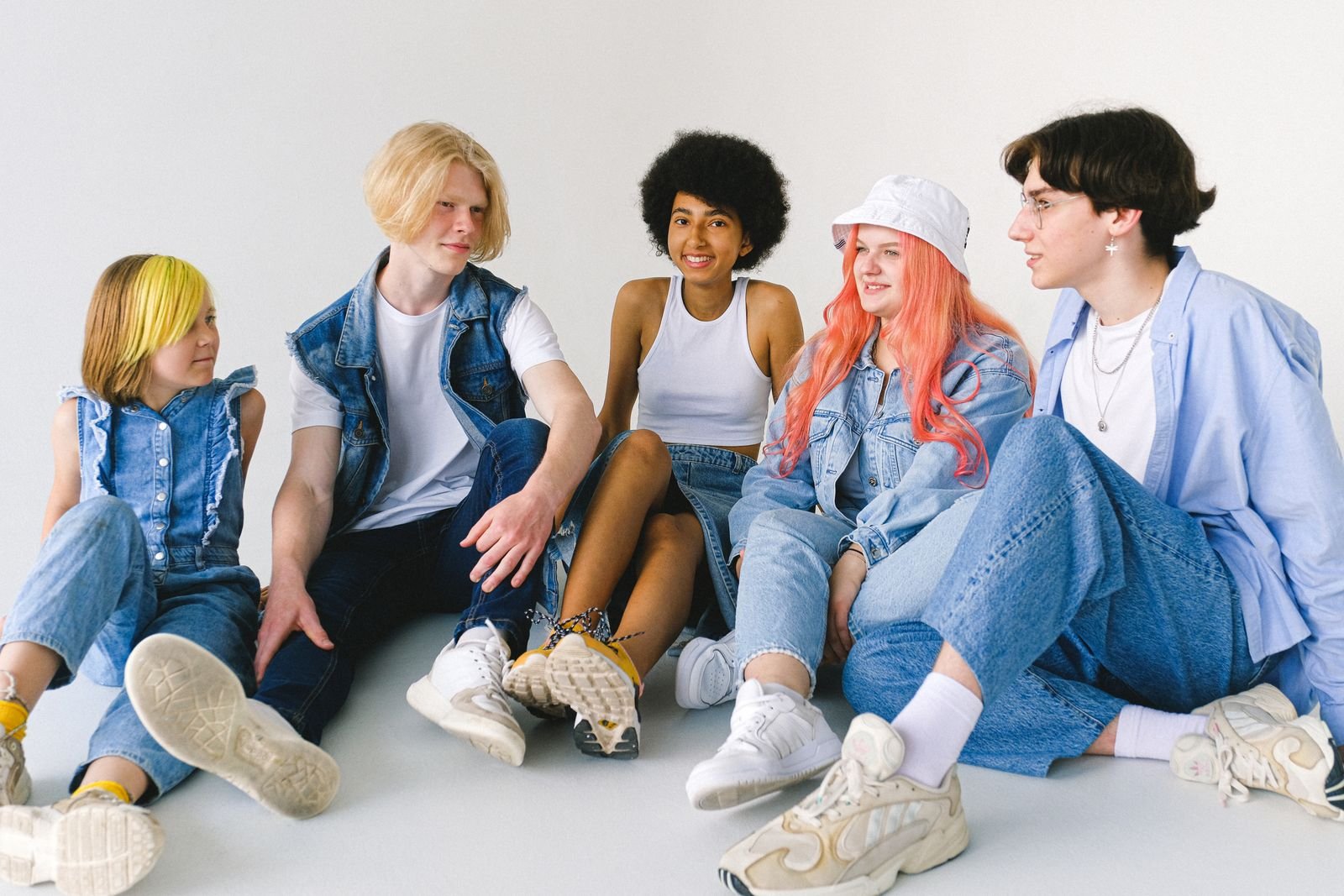 Five teenagers sitting together in layered denim outfits, a bucket hat and chunky sneakers, showing a Y2K-inspired look