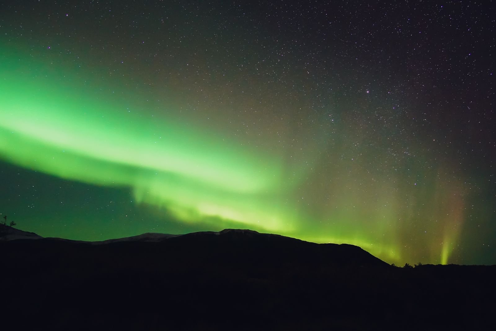 Bright green northern lights arching across a starry night sky above a dark mountain silhouette