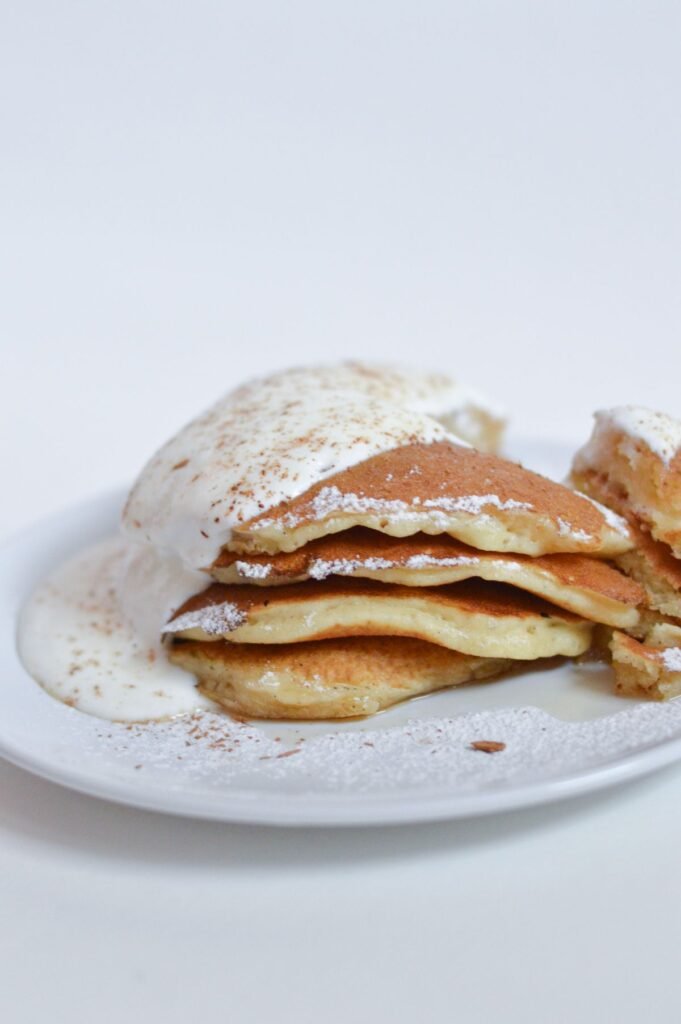 Stack of pancakes topped with white icing and a dusting of cinnamon on a white plate