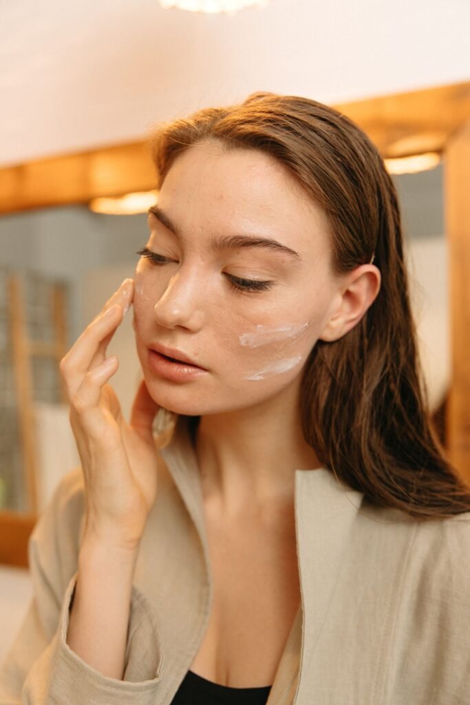 Woman applying a light layer of cream to her cheek in front of a mirror